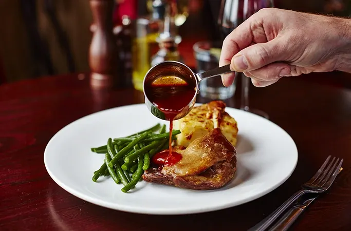 Sauce being poured over Confit de Canard