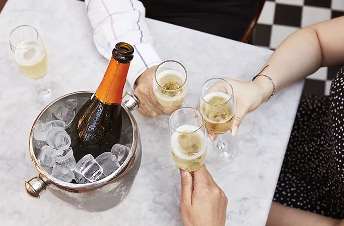 Hands holding glasses of bubbles next to a bottle in an ice bucket