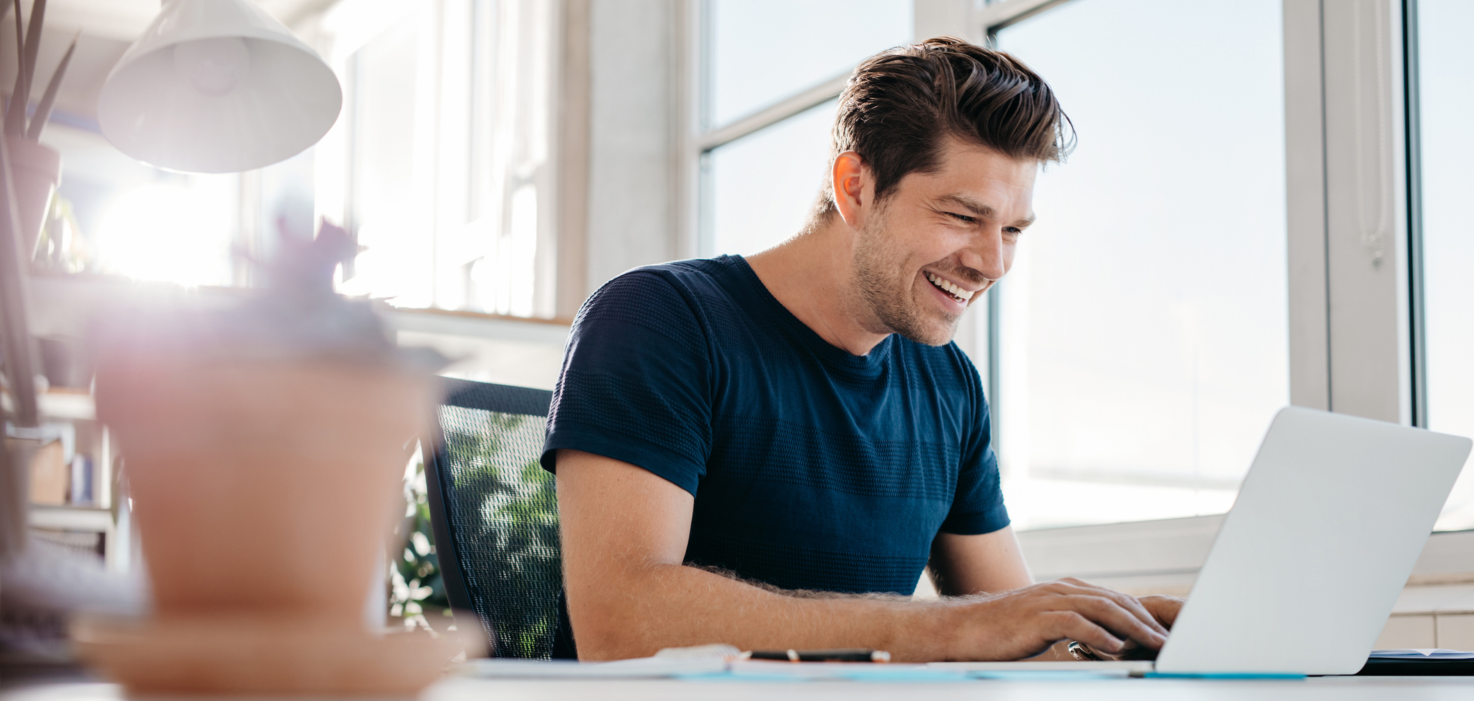 Een man zit in het thuiskantoor aan zijn bureau naast een groot raam