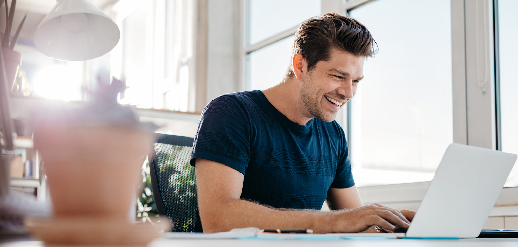 Een man zit in het thuiskantoor aan zijn bureau naast een groot raam