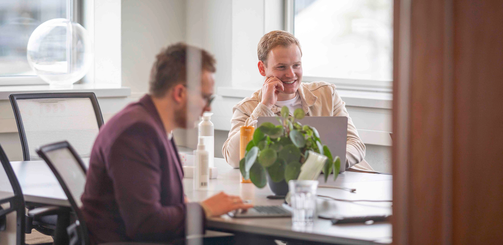 Twee collega's (Leander en Ron) hebben een meeting met thuiswerkers in een meeting ruimte. 