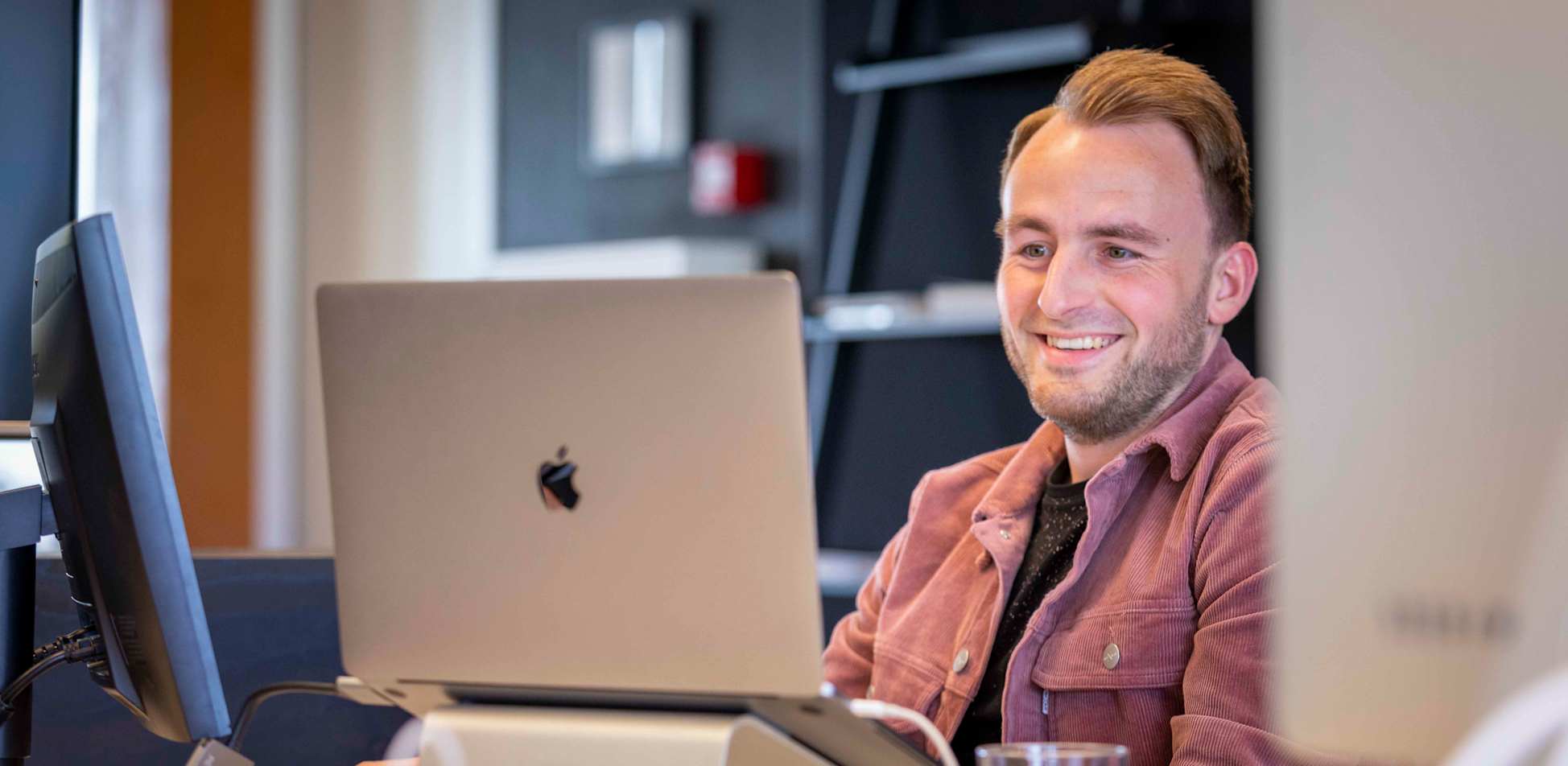 Boy, UI/UX Designer, zit lachend aan een bureau te werken. 