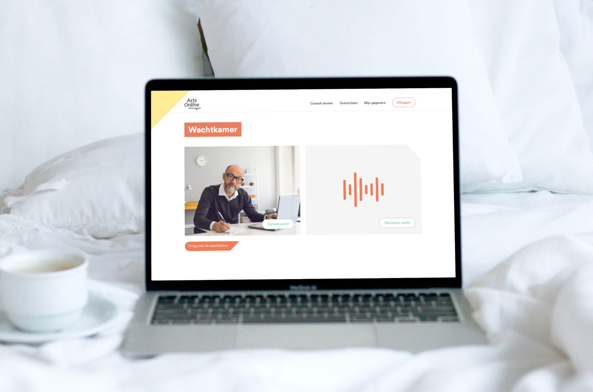 ArtsOnline - Een laptop met de website in een bed met witte lakens en een tas koffie.