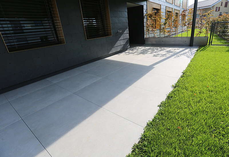 Dalles de trottoir en grès cérame fin de couleur grise pour une terrasse au rez-de-chaussée.