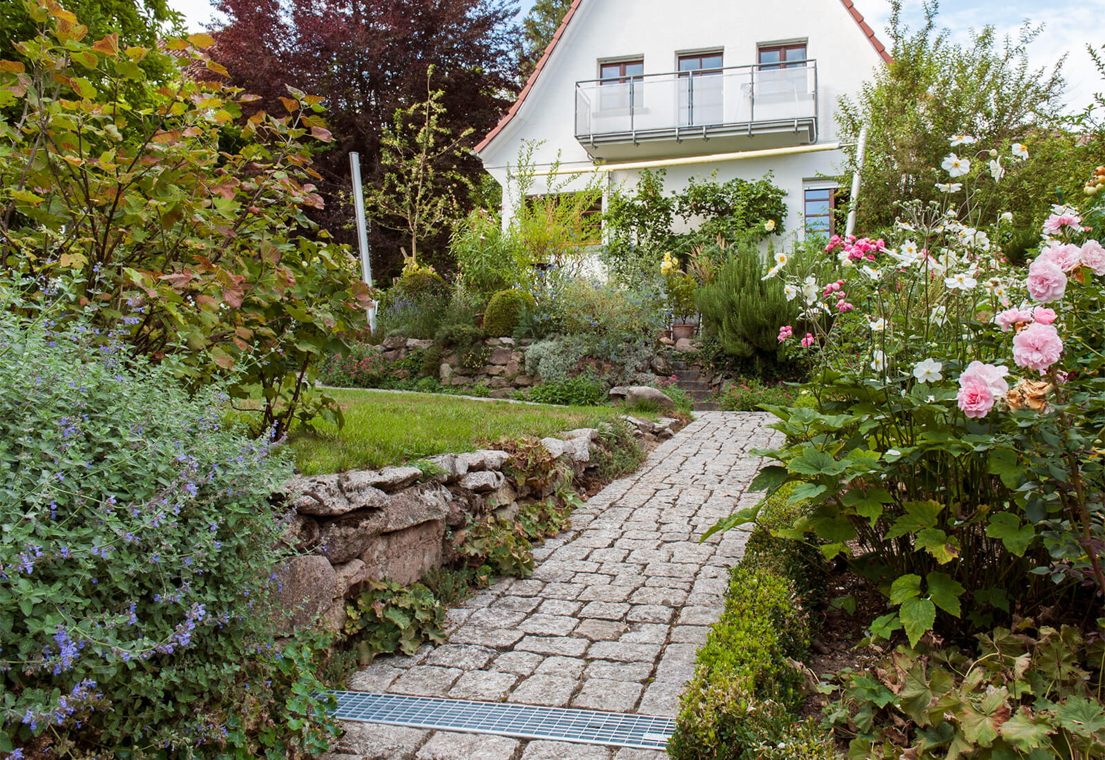 Entwässerungsrinne bei einem Gehweg vor einem Einfamilienhaus mit blühendem Garten