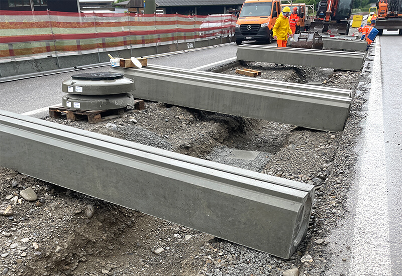 Eine Baustelle auf einer Autobahn wo Schlitzrinnen aus Beton bereit für den Einbau auf dem Kiesboden liegen. 