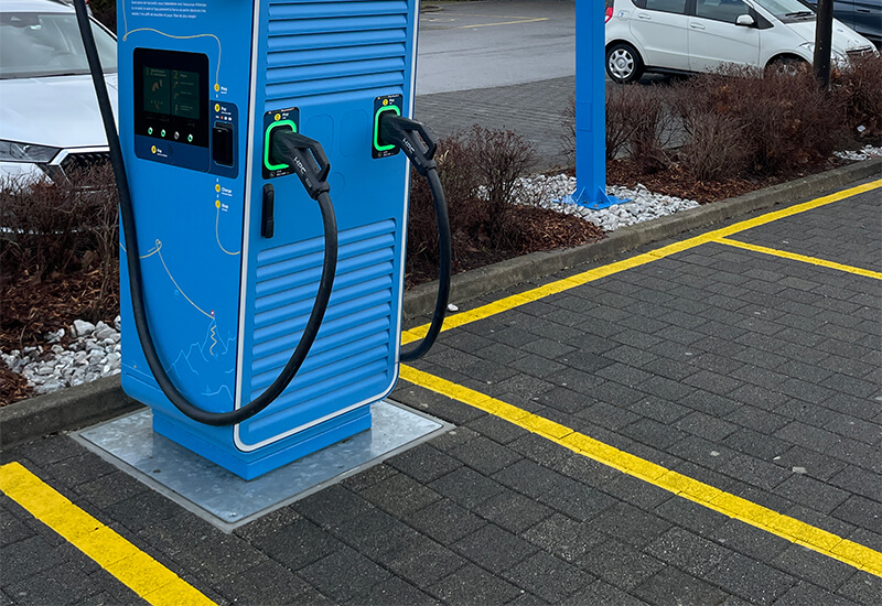 Nahaufnahme einer blauen GOFAST-Elektroauto-Ladestation, die fest auf einer silbernen Metallplatte im Boden verankert ist.