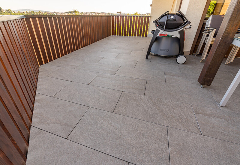 Dalles de trottoir en grès cérame fin couleur sable sur un balcon asymétrique.