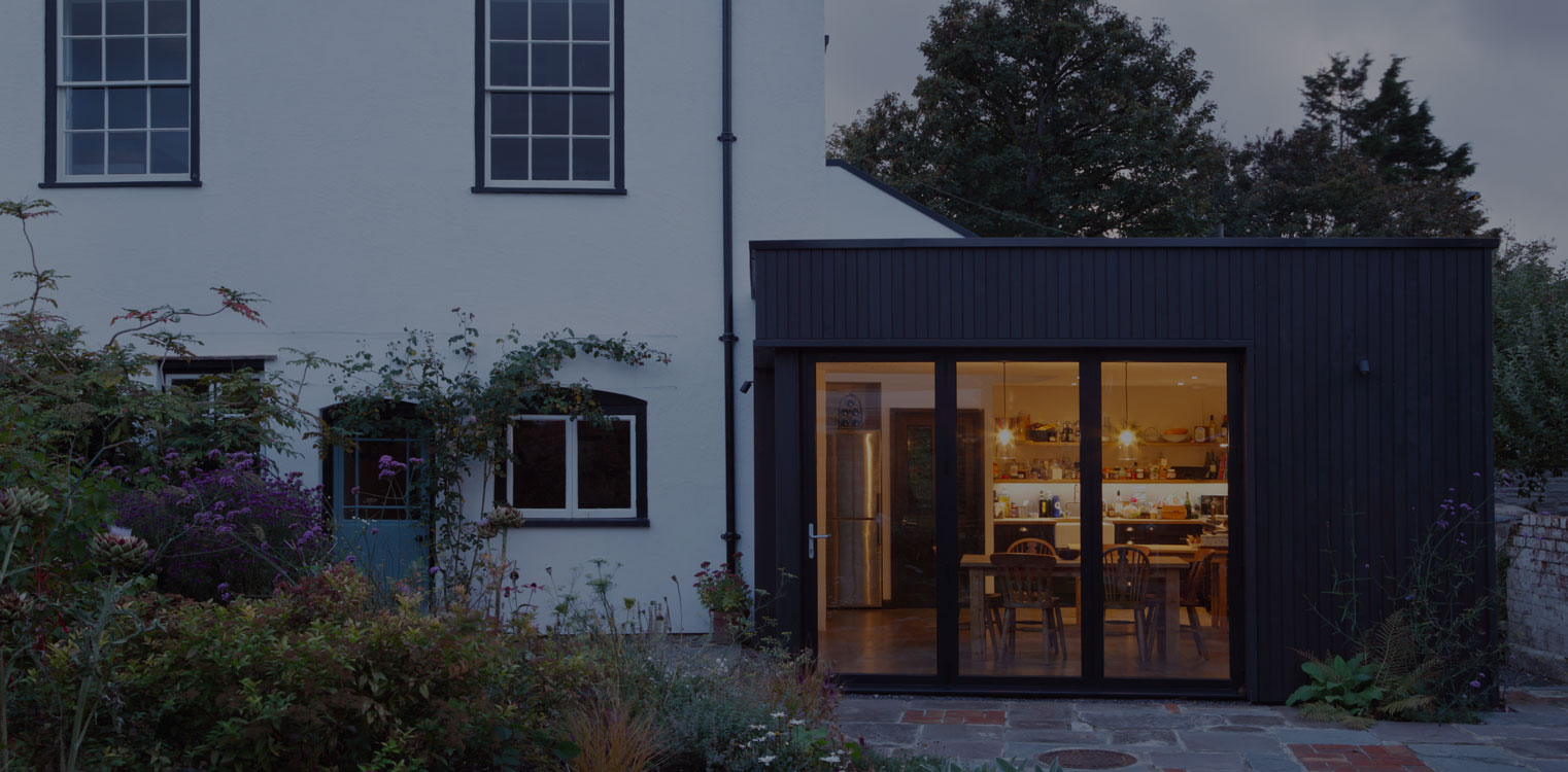 Windows and Doors A hero A house with modern, dark coloured extension that shows large glass windows that reveals a brightly lit interior