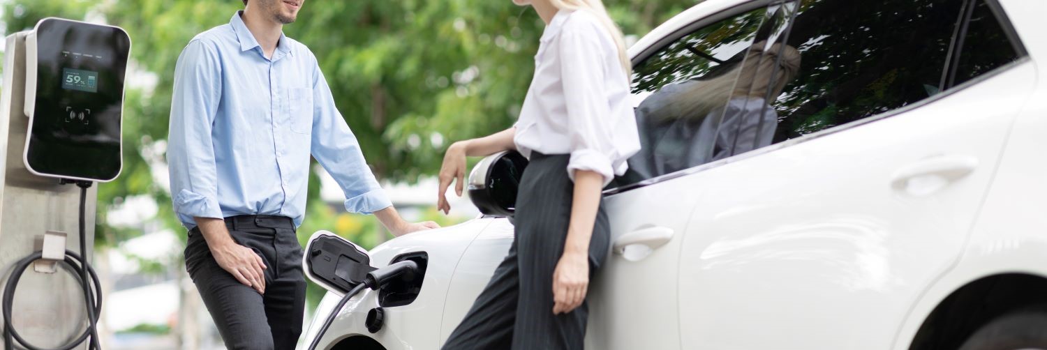 A man and a woman talking beside a charging electric car