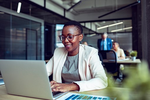 A woman working on a laptop smiling in an office environment 