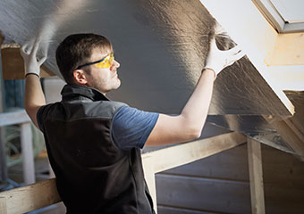 Smart Hints & Tips: Generation Green Home Upgrade IE HE A man wearing a dark vest, light-colored shirt, safety glasses, and gloves working in an attic
