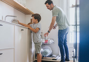 Smart Hints and Tips: Energy Efficiency IE HE A boy rinsing a dish at the sink while a man stands in front of a dishwasher, placing plates inside
