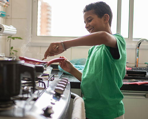 A boy stirring a pot on a gas hob