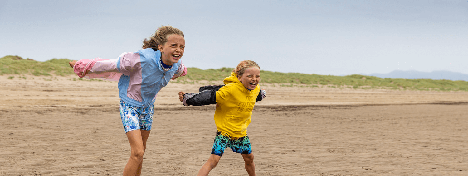 Two girls on a sandy beach, facing the wind with their arms stretched out