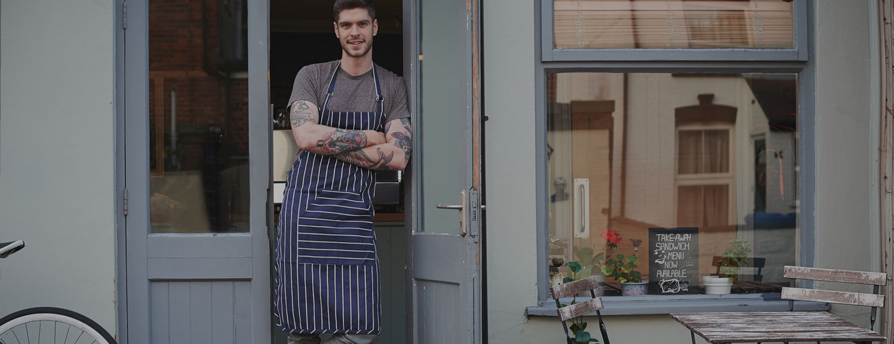 SME-Hero A man wearing a grey top and an apron standing in front of his building
