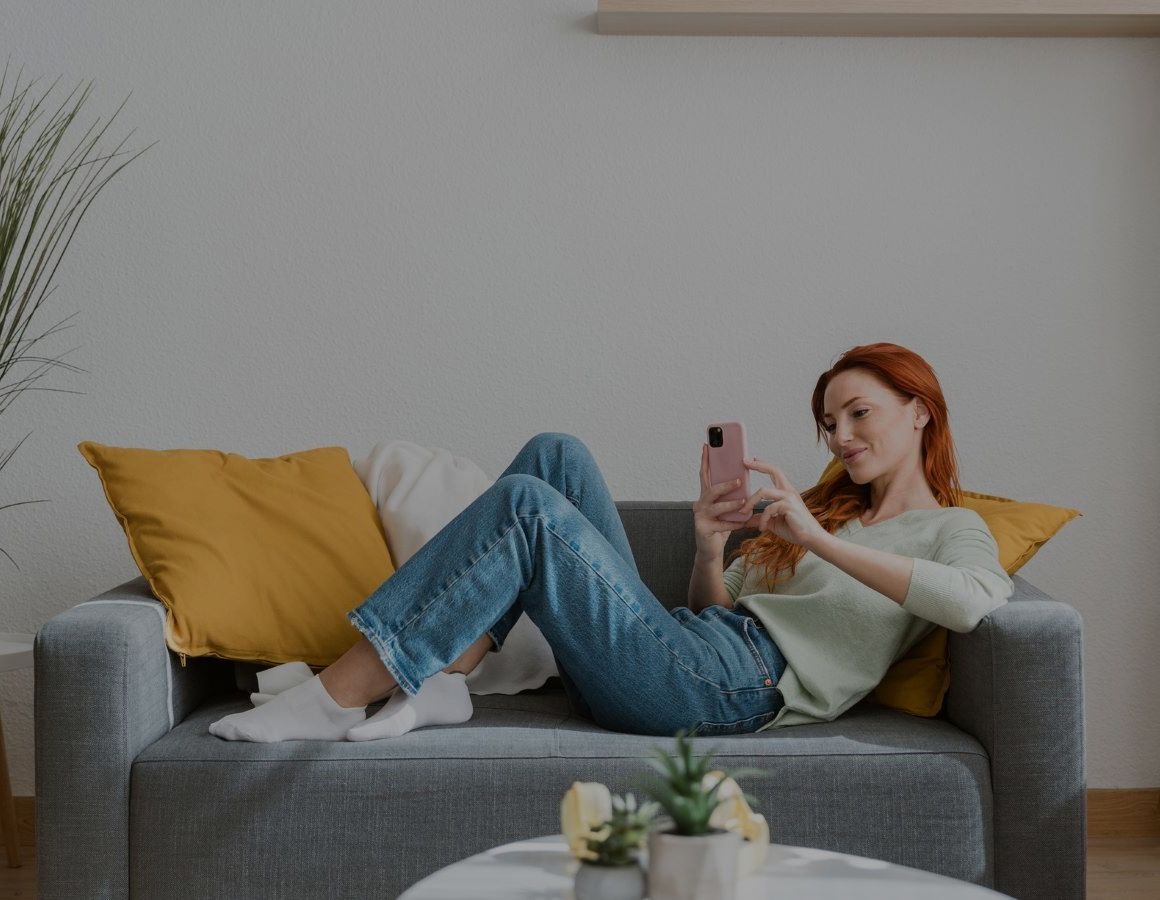 Image directing people to Smart Hub (with overlay) Woman with smart phone sitting on sofa in cosy looking room