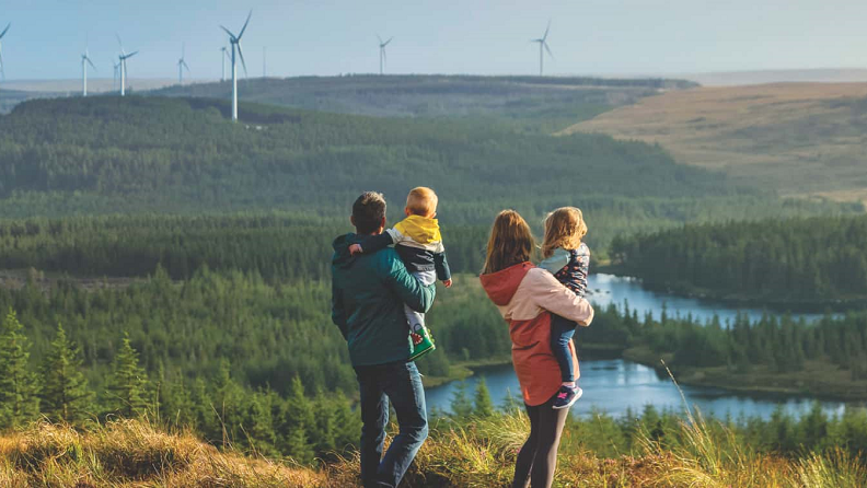 A man and a woman with two children standing in a windmill field.