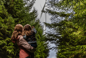 Smart meters for a greener Ireland A mom and her daughter in a forest, with the girl pointing toward a windmill in the distance