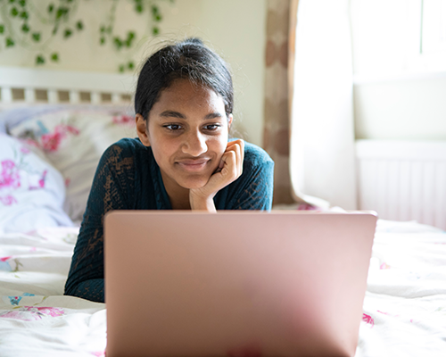 A teenage girl lying on her bed with her laptop