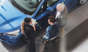 An overhead image of a blue electric car with three people standing outside of it.