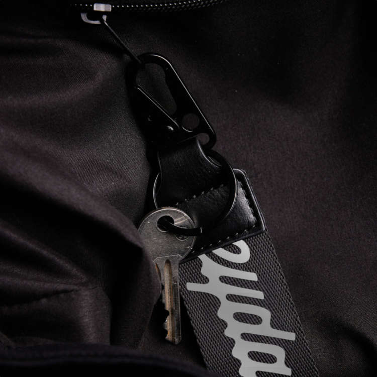 A black EYDA keychain clipped to a zipper