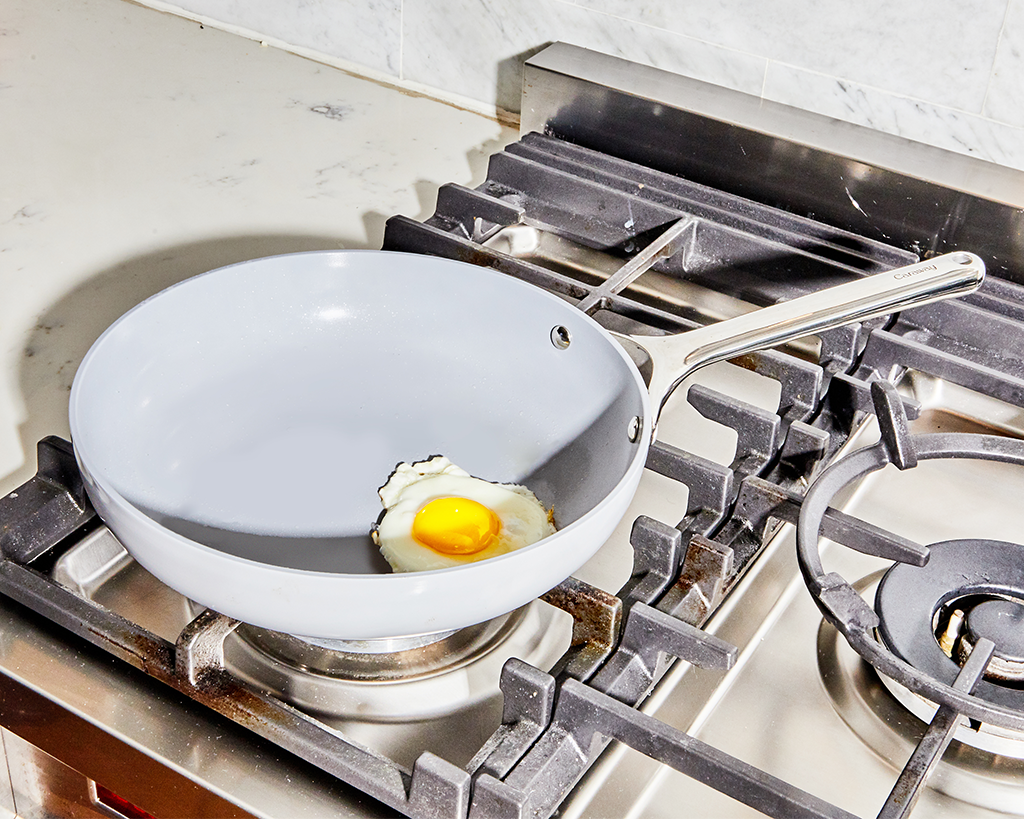 A white ceramic non-stick fry pan being used to cook an egg