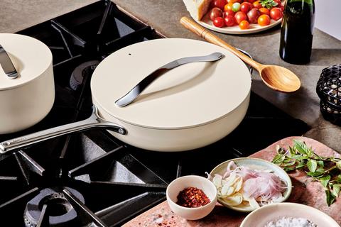 A ceramic white non-stick sauté pan resting on a stove top with a lid on