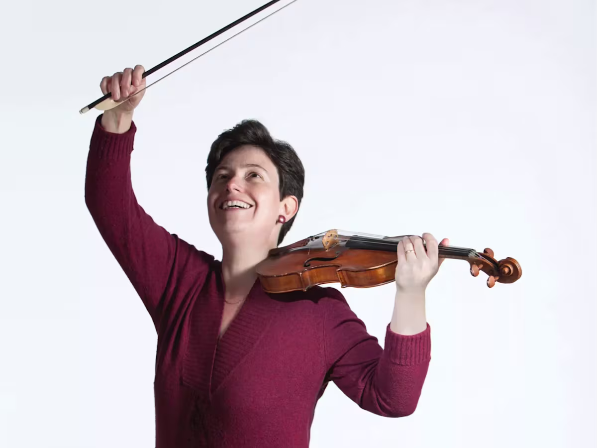 a woman Katia Debretzeni holding a violin and bow as if she has just finished performing