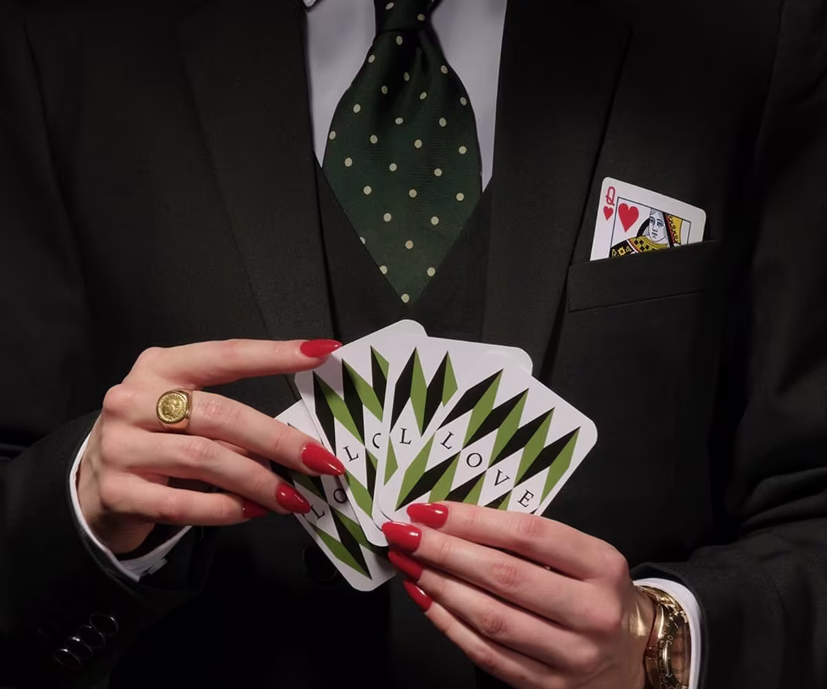 Handel: Partenope a woman with red nail varnish and a smart black suit and tie holds a pack of cards close to her chest