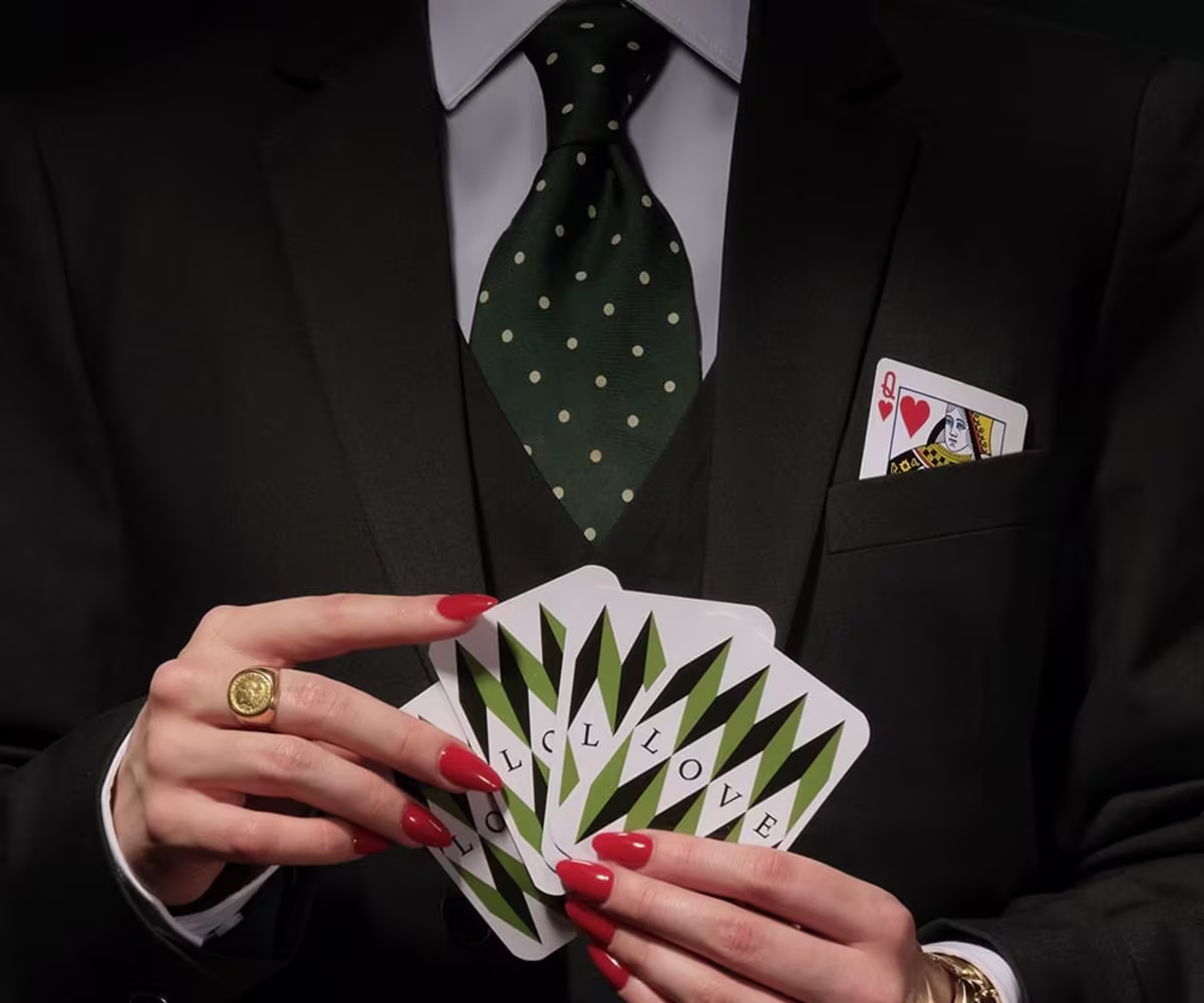 Partenope a woman with red nail varnish and a smart black suit and tie holds a pack of cards close to her chest