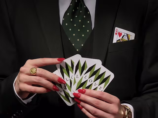 Handel: Partenope a woman with red nail varnish and a smart black suit and tie holds a pack of cards close to her chest