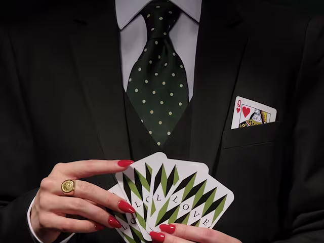 Handel: Partenope a woman with red nail varnish and a smart black suit and tie holds a pack of cards close to her chest