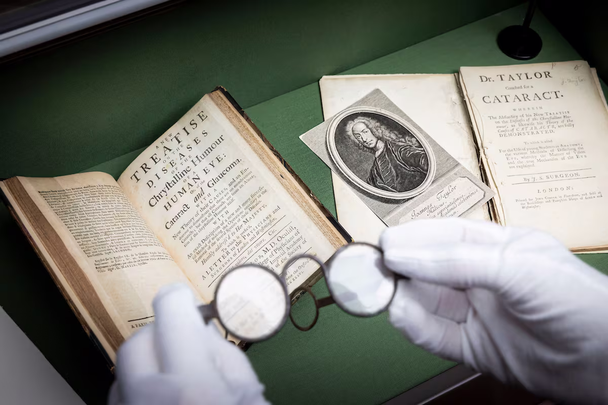 A member of staff holds a pair of period spectacles in front of a book by notorious quack John Taylor | photo by Christopher Ison c/o Handel Hendrix House A member of staff holds a pair of period spectacles in front of a book by notorious quack John Taylor | photo by Christopher Ison c/o Handel Hendrix House