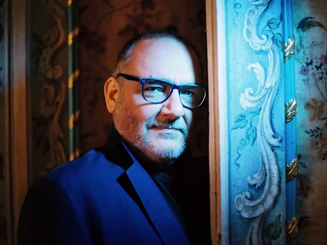 Concerto Italiano a man peering from behind an ornage door in moody lighting