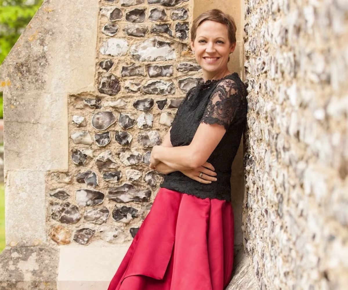 Purcell’s Dido and Aeneas julia doyle mezzo soprano leaning against a flint church all wearing a red skirt