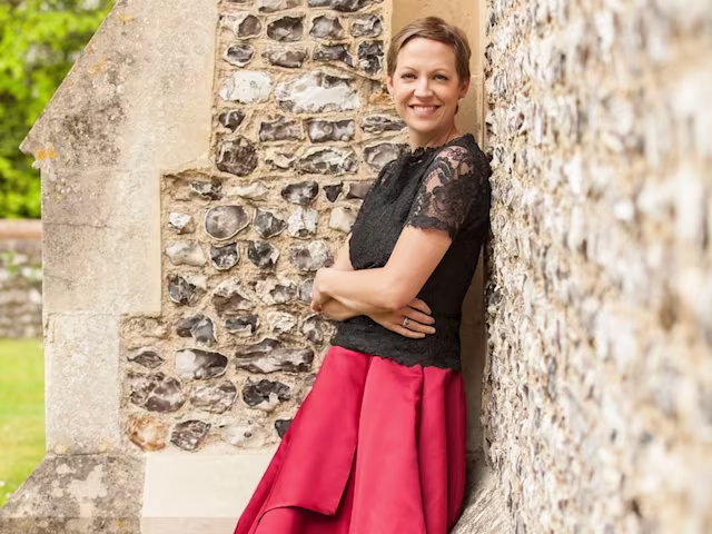 Purcell’s Dido and Aeneas julia doyle mezzo soprano leaning against a flint church all wearing a red skirt