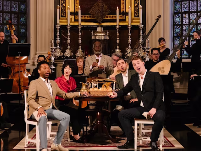 Bach's Markus Passion singers and historical instrumentalists sit around a table performing in a church