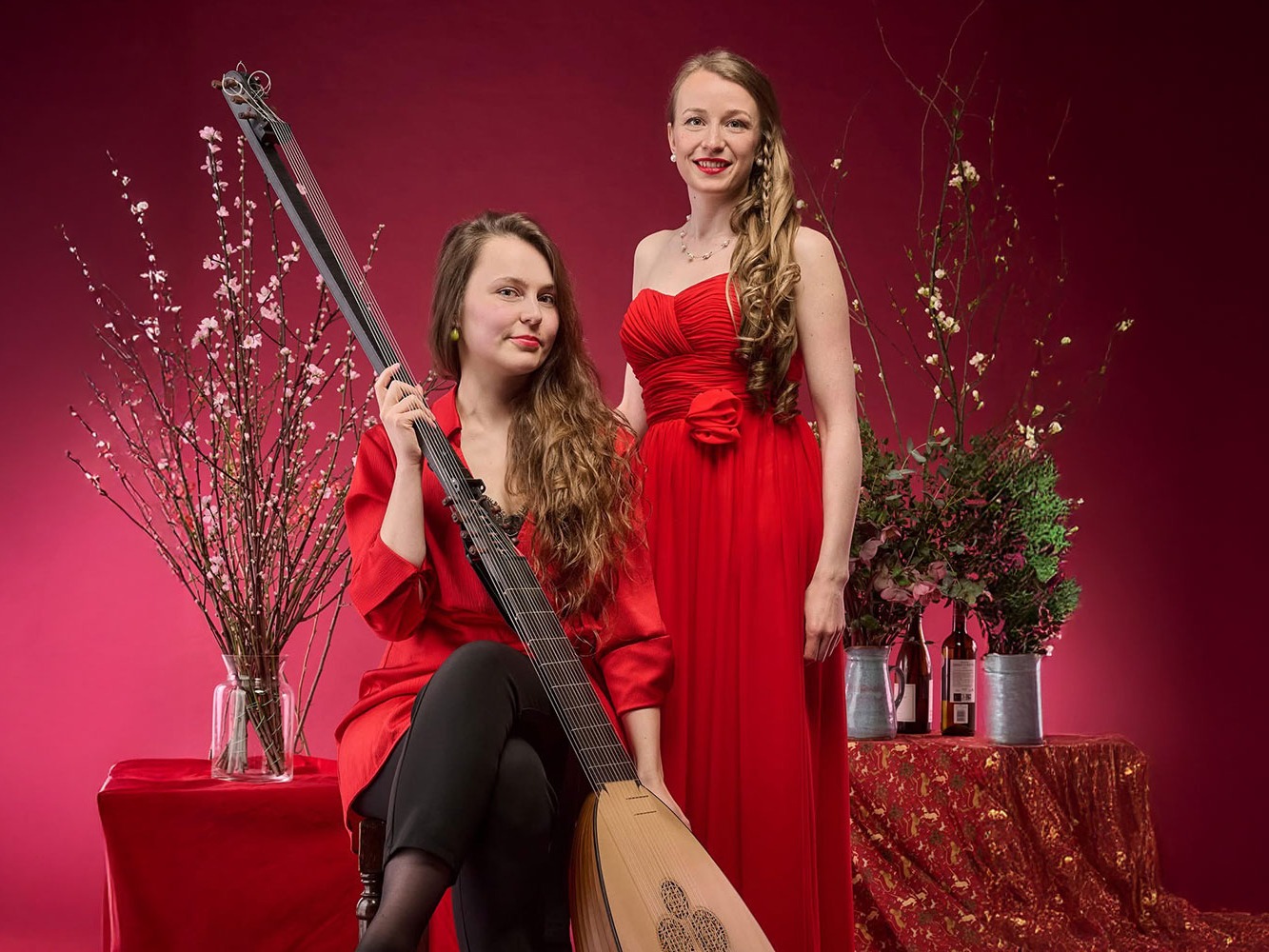 soprano angela hicks and lutenist kristiina watt wearing red dresses with a festive background