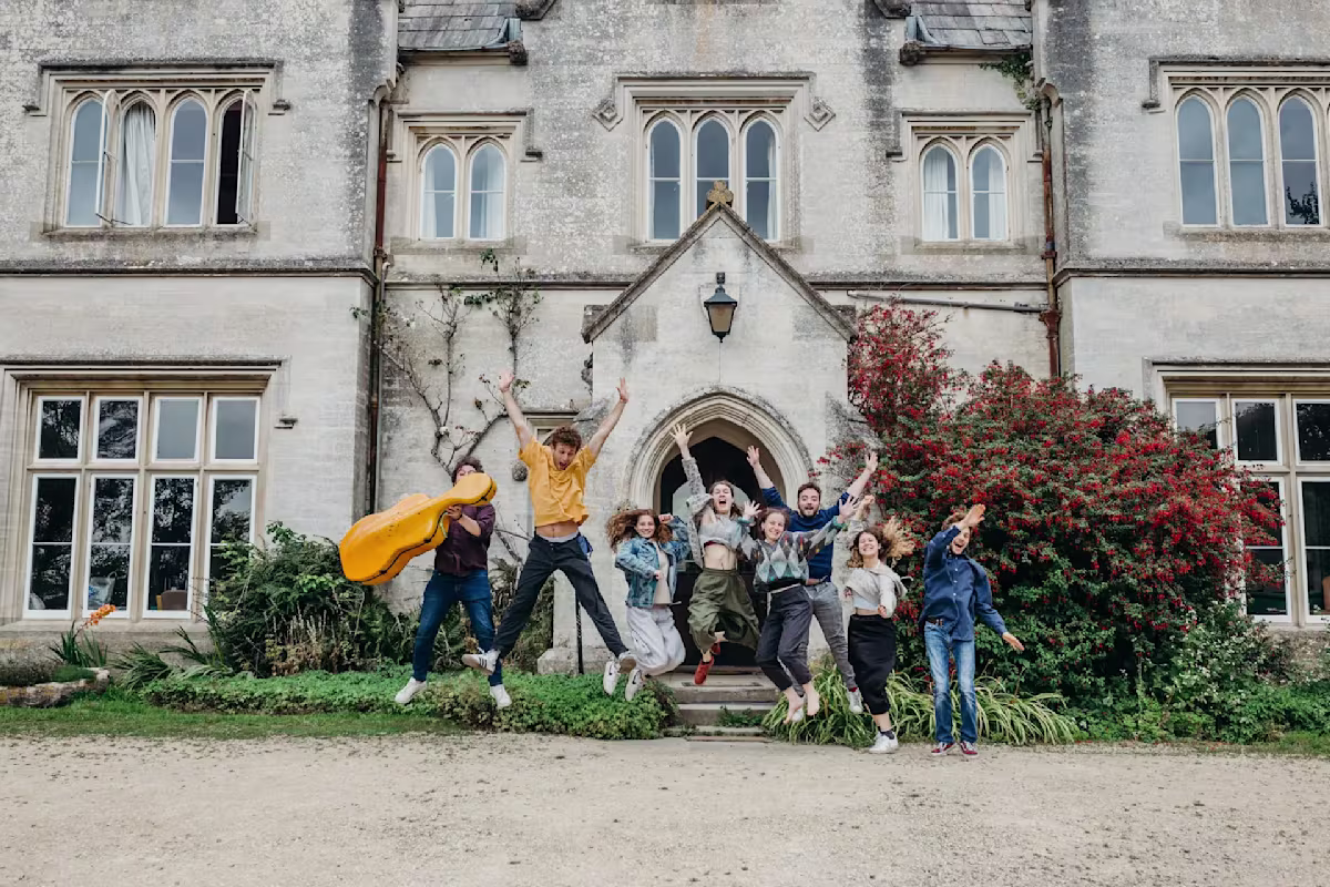 Hawkwood College a group of young people jumping in the air in front of an old country house hawkwood in gloucestershire