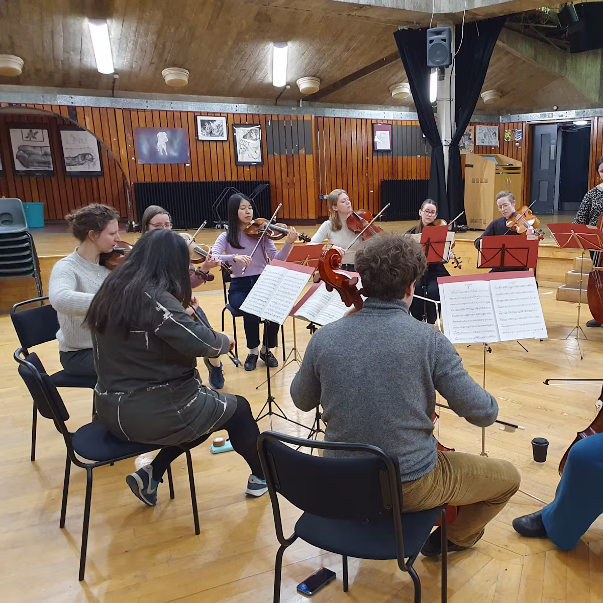 Applications open for prestigious orchestral experience scheme classical musicians sitting in a circle in a large rehearsal space with wooden floors and walls