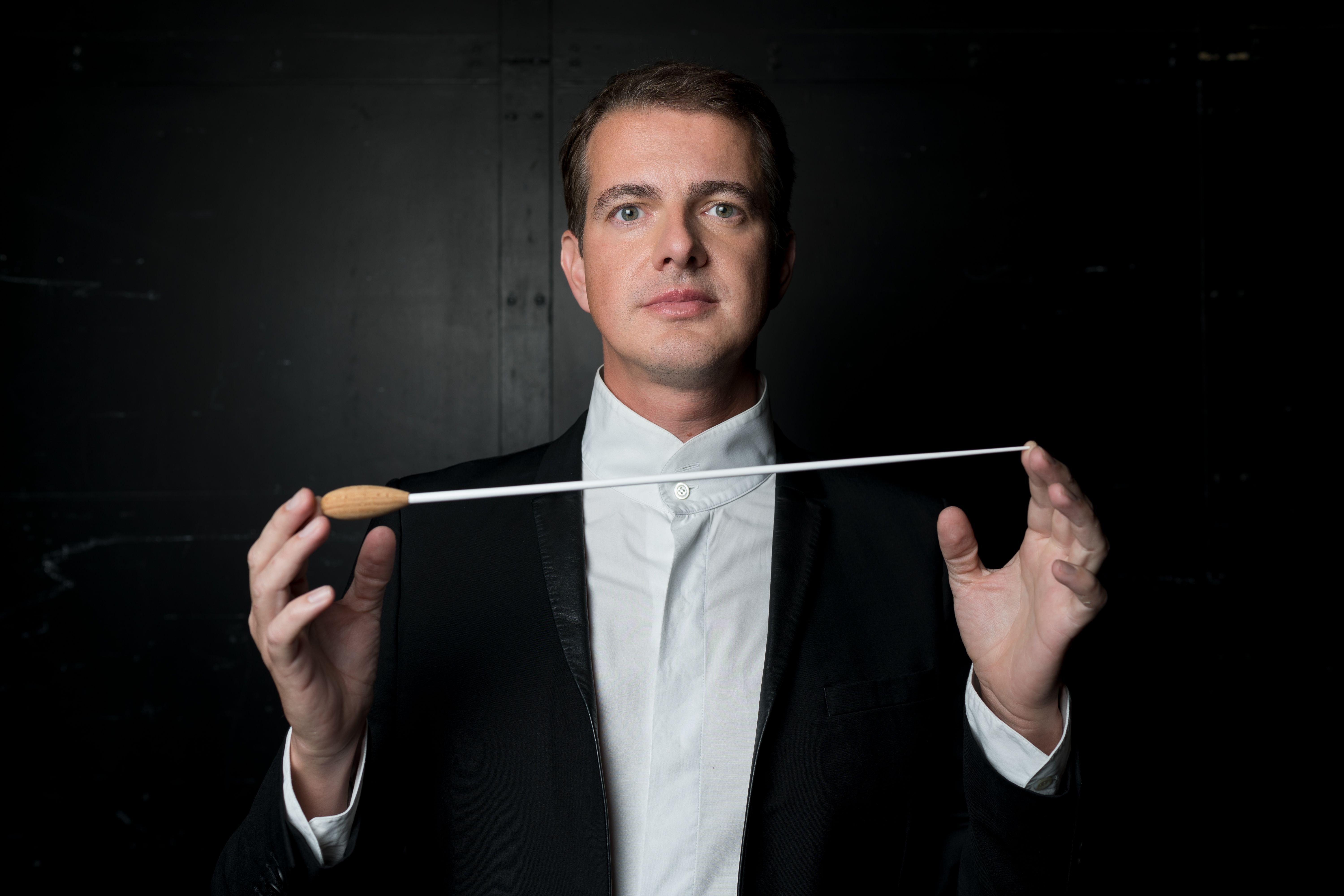 A conductor Philippe Jaroussky in a tailcoat holding a baton between his hands