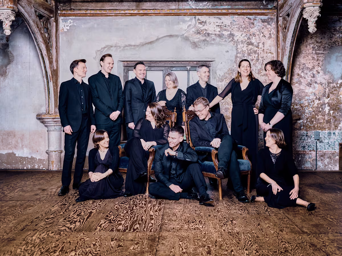 singers from stile antico wearing all black grouped together in front of an old wall with wallpaper peeling off