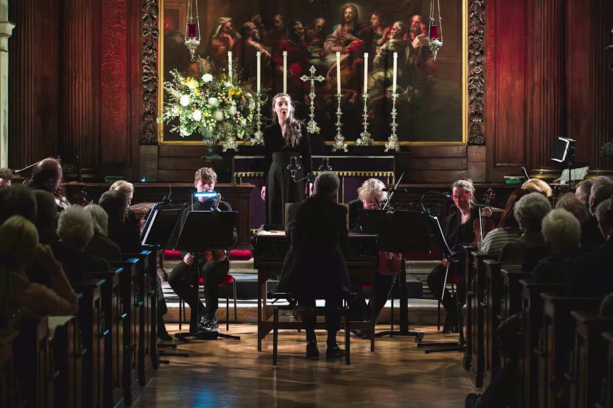 a woman sings baroque music in an ornate church setting with a small orchestra in front of her