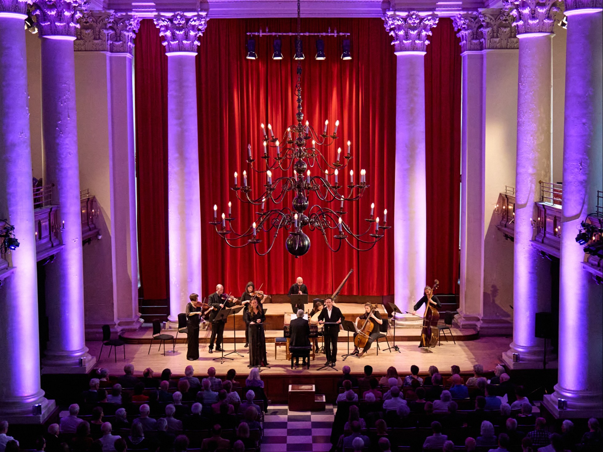 Musicians performing on stage of Smith Square Hall in London with purple atmospheric lighting framing the pillars behind the stage