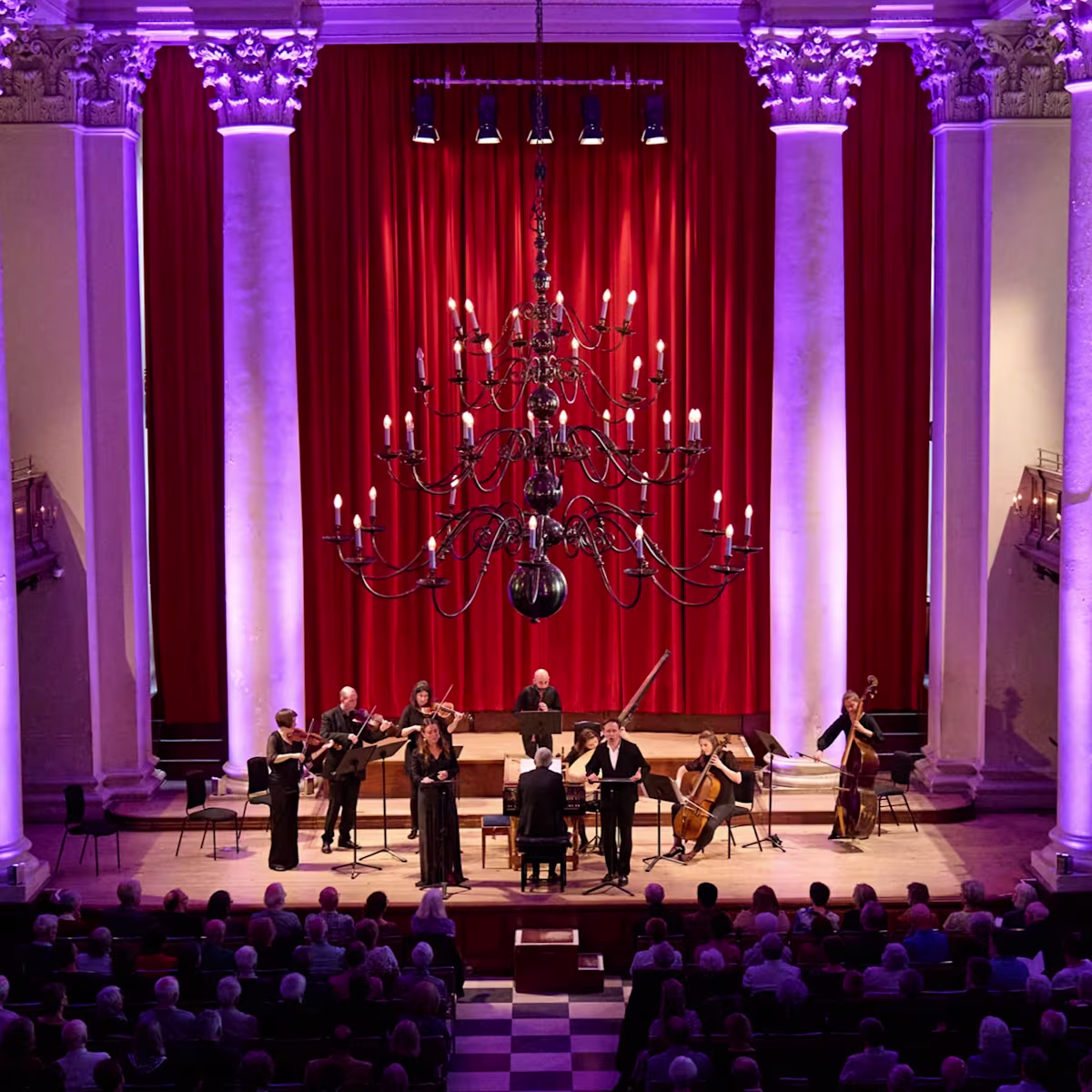 London Festival of Baroque Music Musicians performing on stage of Smith Square Hall in London with purple atmospheric lighting framing the pillars behind the stage