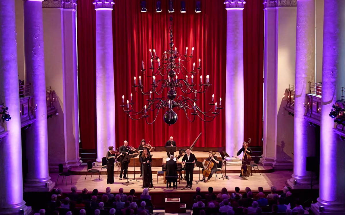 LFBM set to take off as British Airways partners with Sinfonia Smith Square Musicians performing on stage of Smith Square Hall in London with purple atmospheric lighting framing the pillars behind the stage