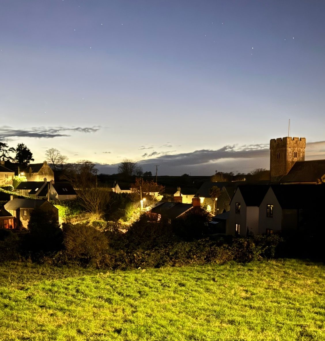 a nighttime vista of a church spire and clear sky with floodlight grass in the foreground