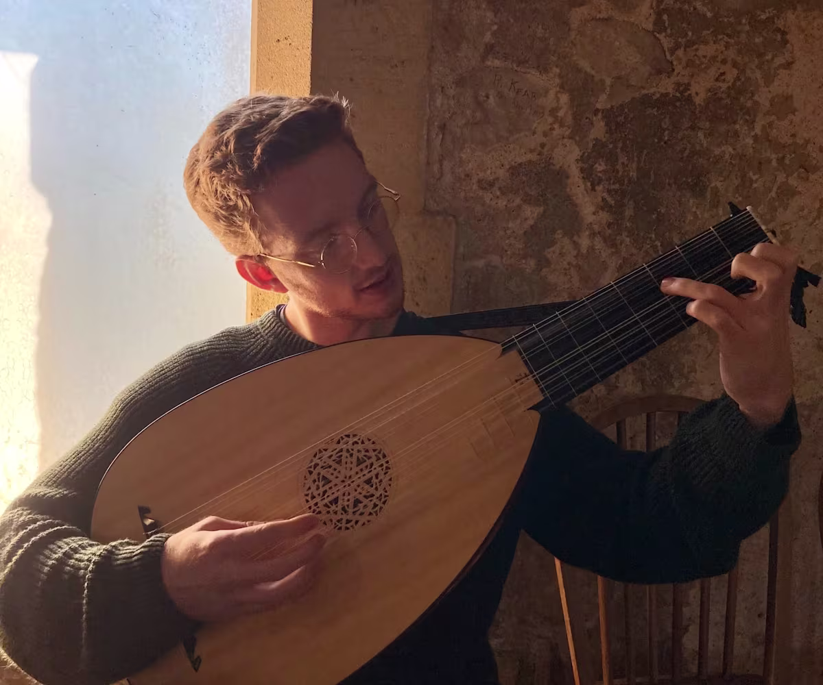 The Last Lute Player a man playing a lute sat on a stone windowsill