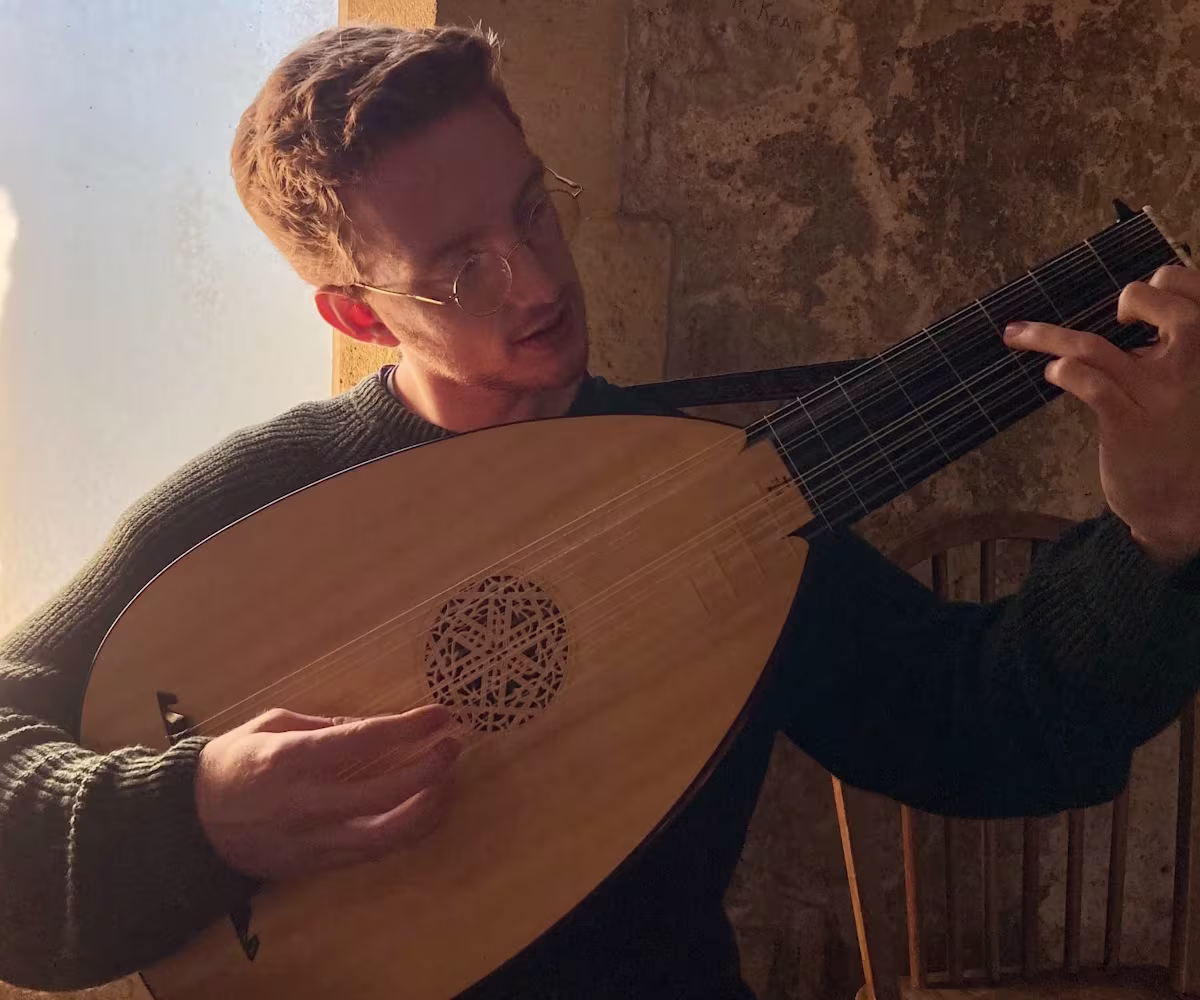 Daniel Murphy a man playing a lute sat on a stone windowsill